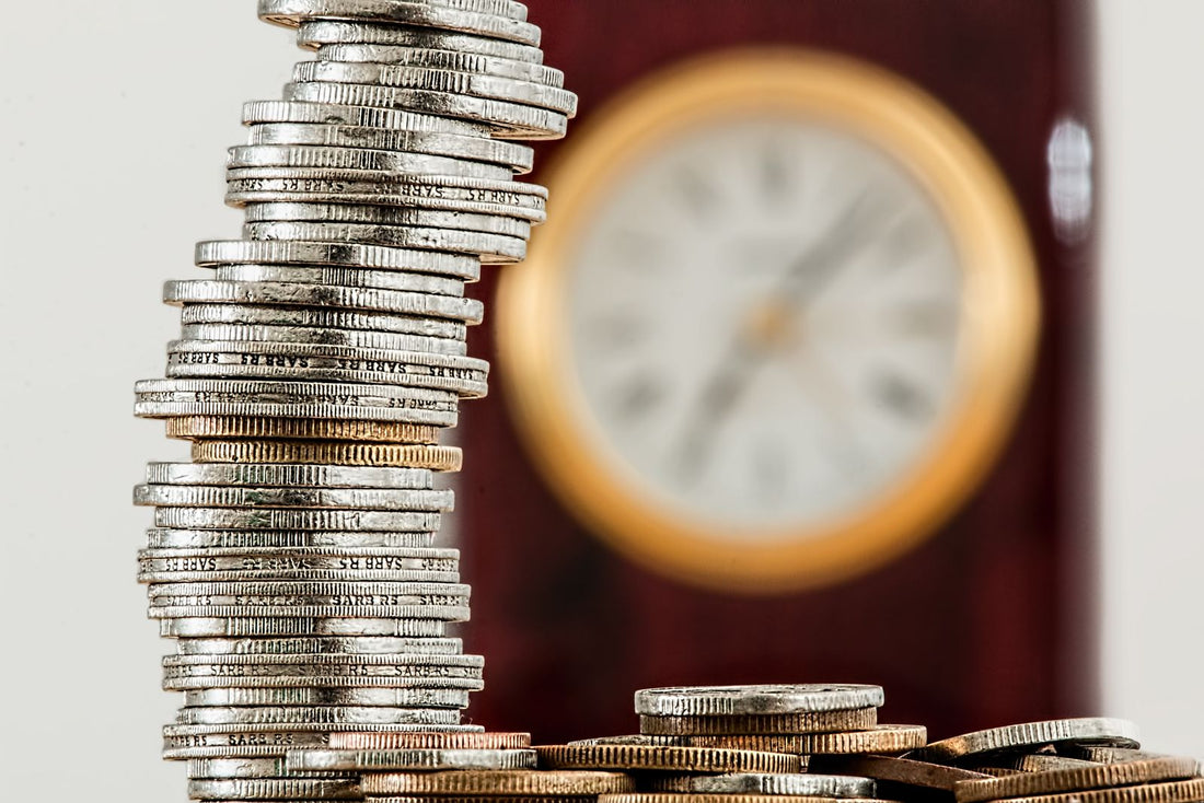Stacked coins in focus with a clock behind