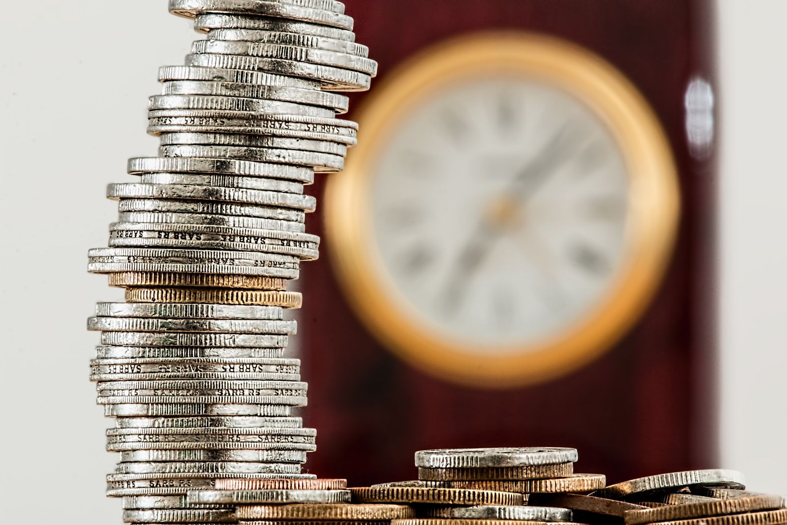 Stacked coins in focus with a clock behind