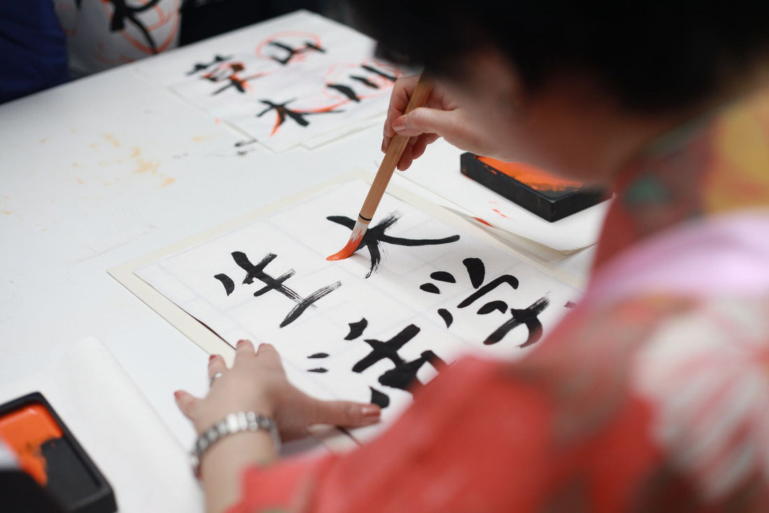 A hand holding a brush drawing kanji script