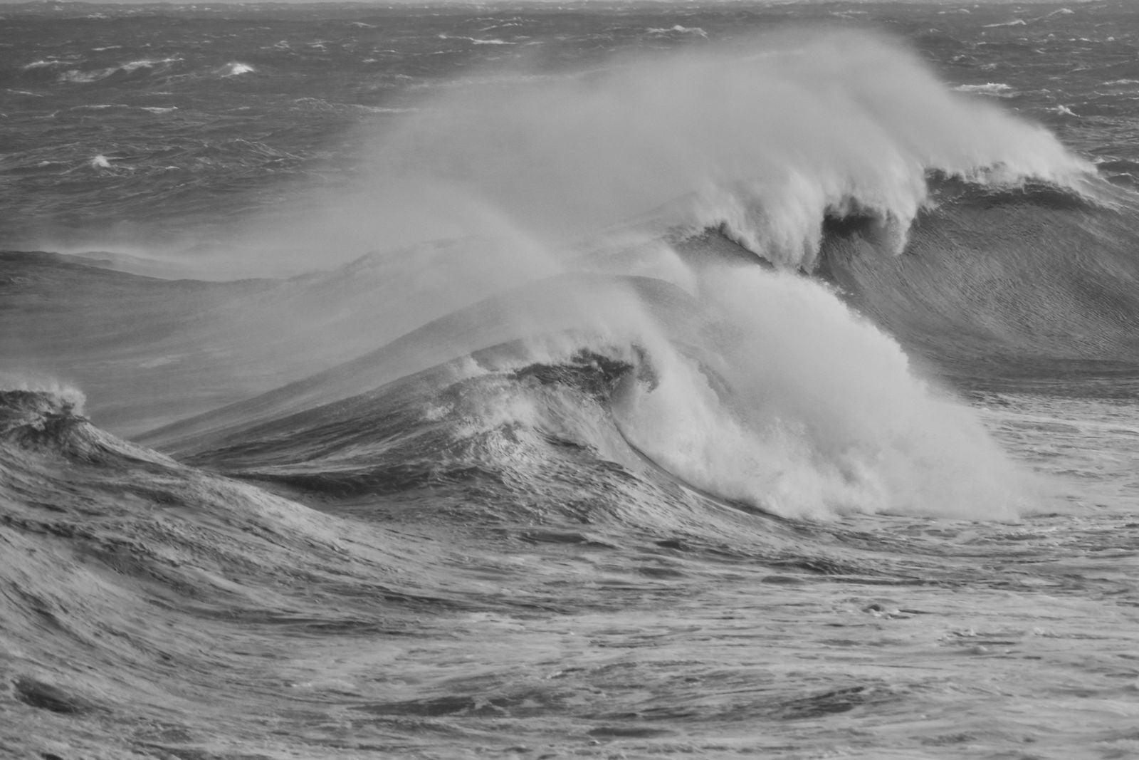 A wave breaking on the shore in black and white