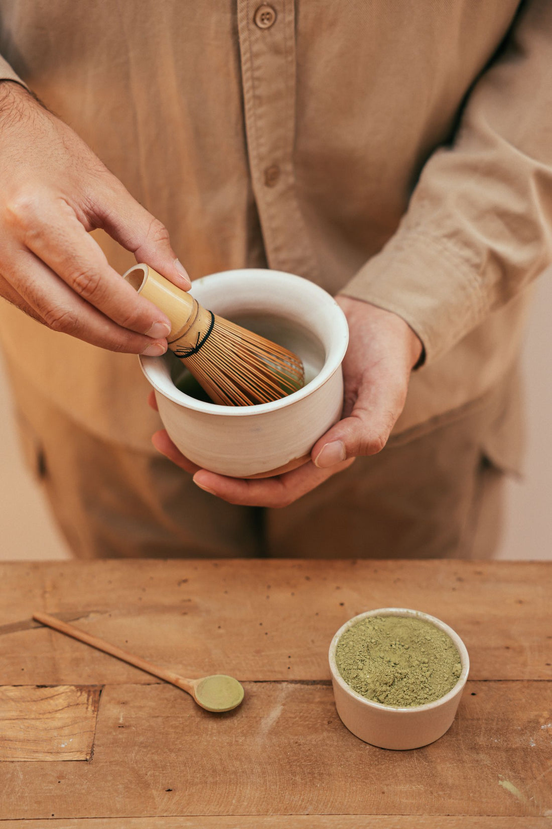 A hand holding a bamboo whisk over a bowl of matcha
