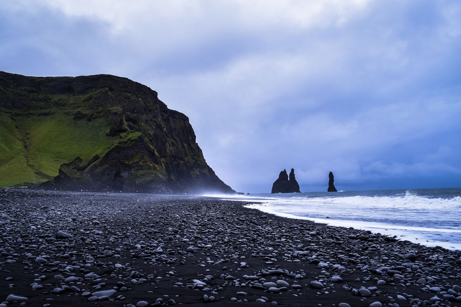 Black sand beach and basalt sea stacks under a grey northern sky